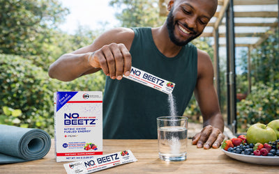Healthy active man pouring NO2U nitric oxide beet powder stick into a clear glass of water outdoors, with N.O. BEETZ supplement box on table, supporting circulation, energy, and fitness lifestyle.