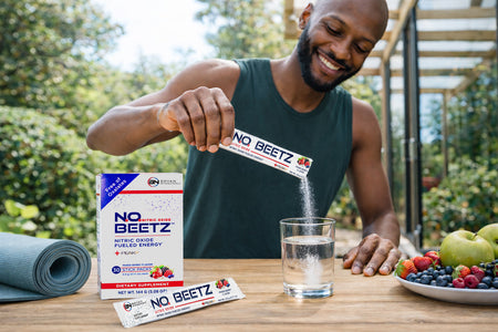 Healthy active man pouring NO2U nitric oxide beet powder stick into a clear glass of water outdoors, with N.O. BEETZ supplement box on table, supporting circulation, energy, and fitness lifestyle.