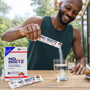 Healthy active man pouring NO2U nitric oxide beet powder stick into a clear glass of water outdoors, with N.O. BEETZ supplement box on table, supporting circulation, energy, and fitness lifestyle.