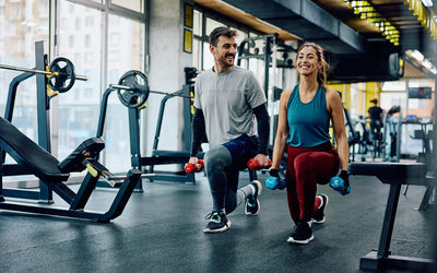 “Man and woman performing walking lunges with dumbbells in a modern gym, illustrating strength training, exercise performance, and nitric oxide production for muscle growth, circulation, and endurance.