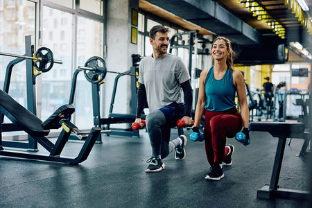 “Man and woman performing walking lunges with dumbbells in a modern gym, illustrating strength training, exercise performance, and nitric oxide production for muscle growth, circulation, and endurance.