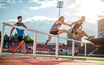 Track athletes sprinting and clearing hurdles on an outdoor stadium track, showcasing speed, endurance, and peak performance supported by nitric oxide for improved blood flow, oxygen delivery, and athletic power.
