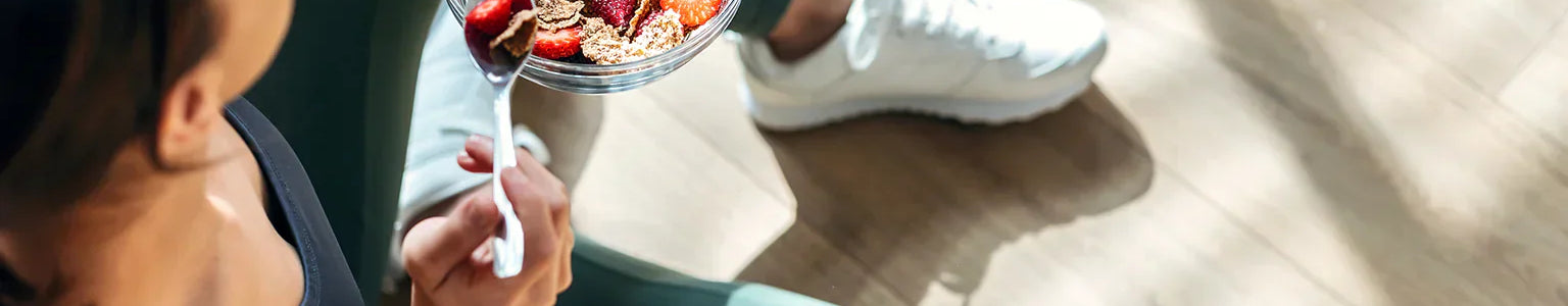 Active woman eating a healthy post-workout bowl with berries and whole grains on the gym floor, highlighting nutrition that supports nitric oxide production, blood circulation, recovery, and overall fitness performance.