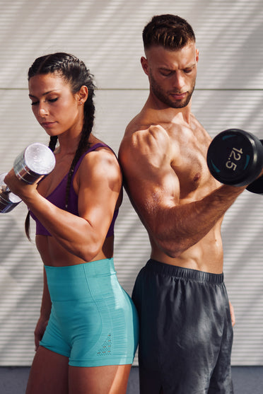 Fit man and woman lifting dumbbells together outdoors, building lean muscle, strength, and athletic performance.