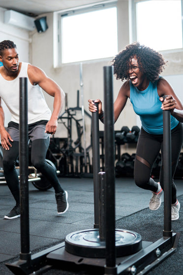 Man and woman pushing weighted sleds during gym workout, improving strength, endurance, and athletic performance.