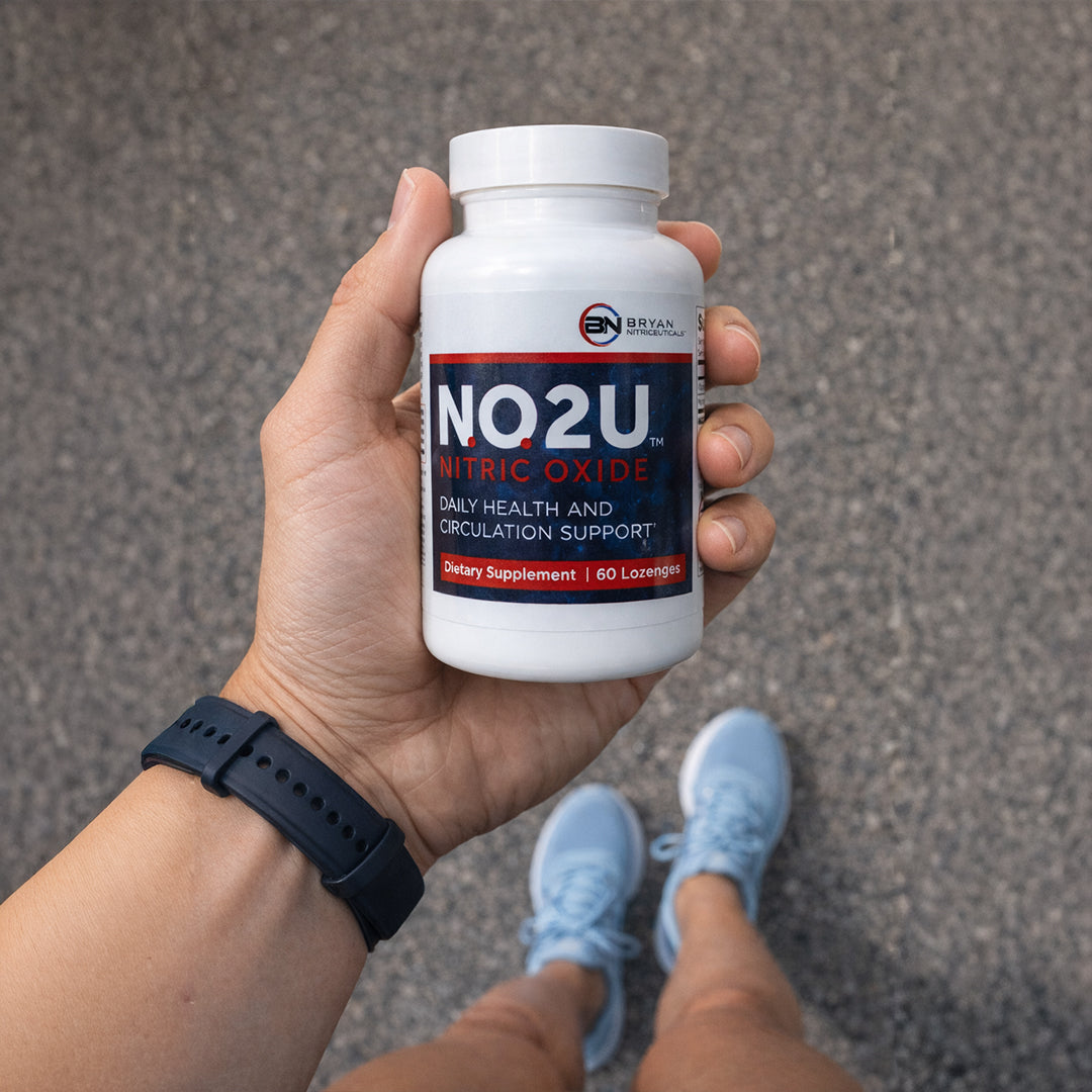 Hand holding a bottle of NO2U Nitric Oxide supplement against a gray pavement background.