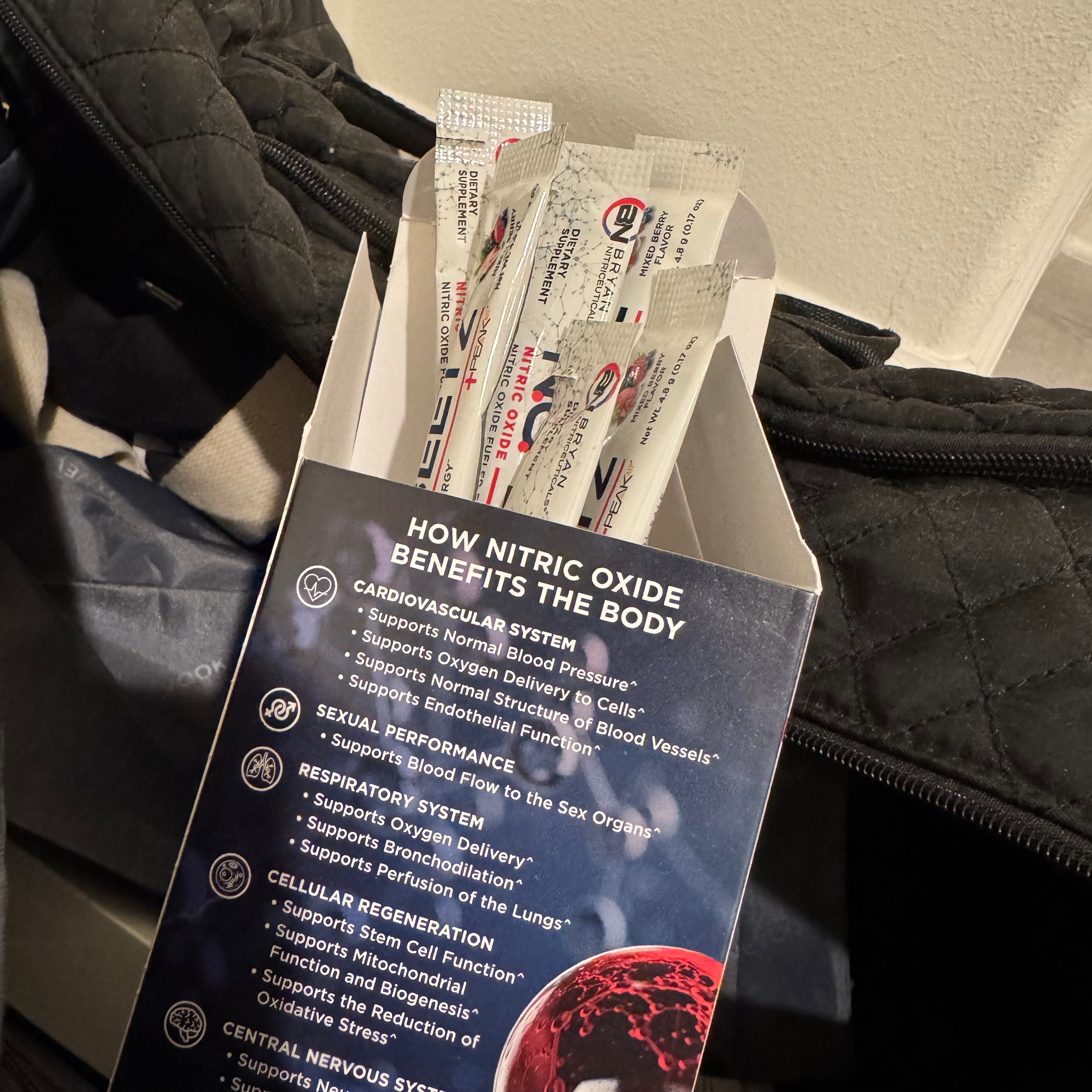 Open box with packets of a supplement or product, showing text about nitric oxide benefits.