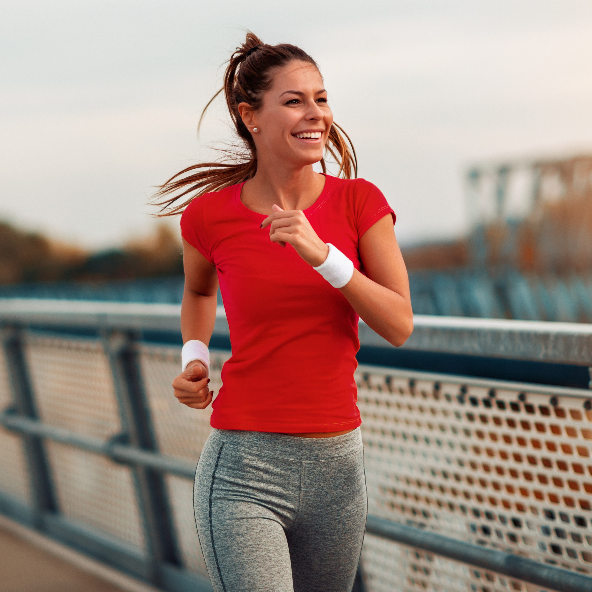 Woman in red shirt and gray leggings jogging on a bridge
