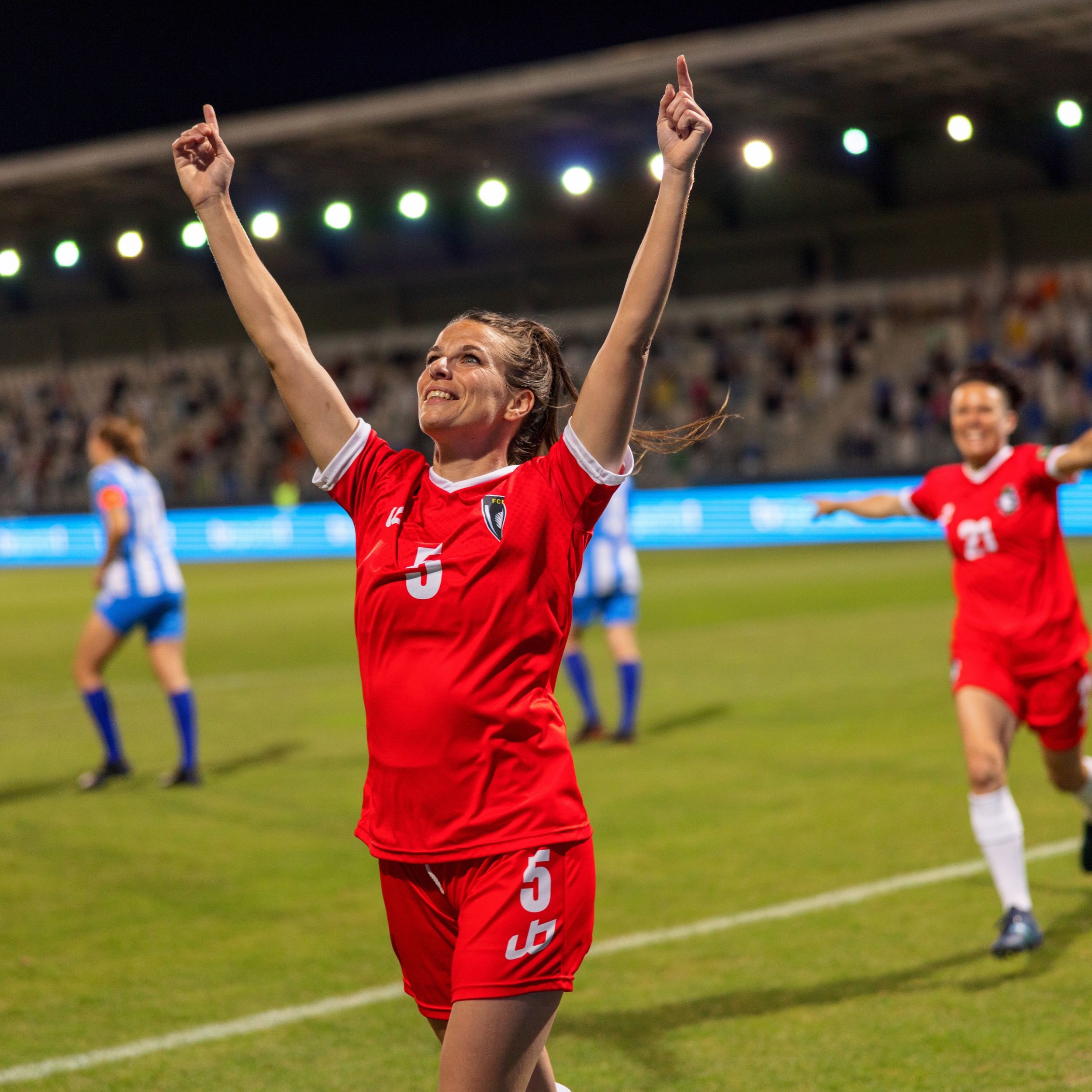 Soccer player in red celebrating on the field with stadium lights in the background