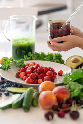 Assorted fruits and vegetables on a table with a glass of juice and a cup.