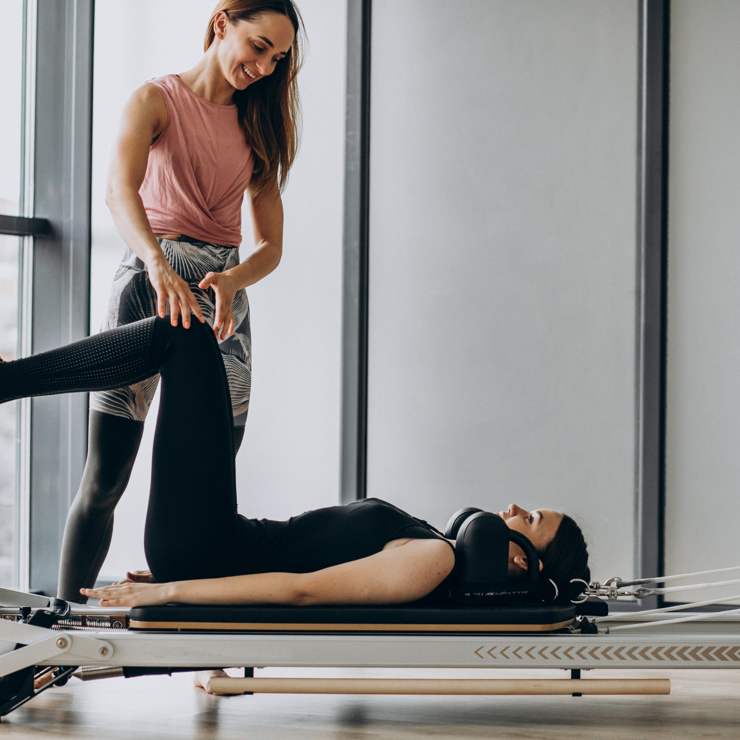 Pilates instructor assisting a client on a reformer machine in a studio setting.